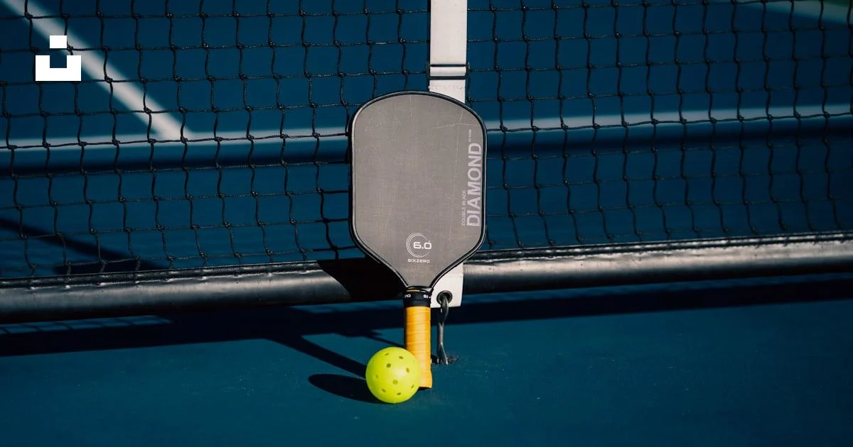 Pickleball paddle and yellow ball beside the net on a blue court